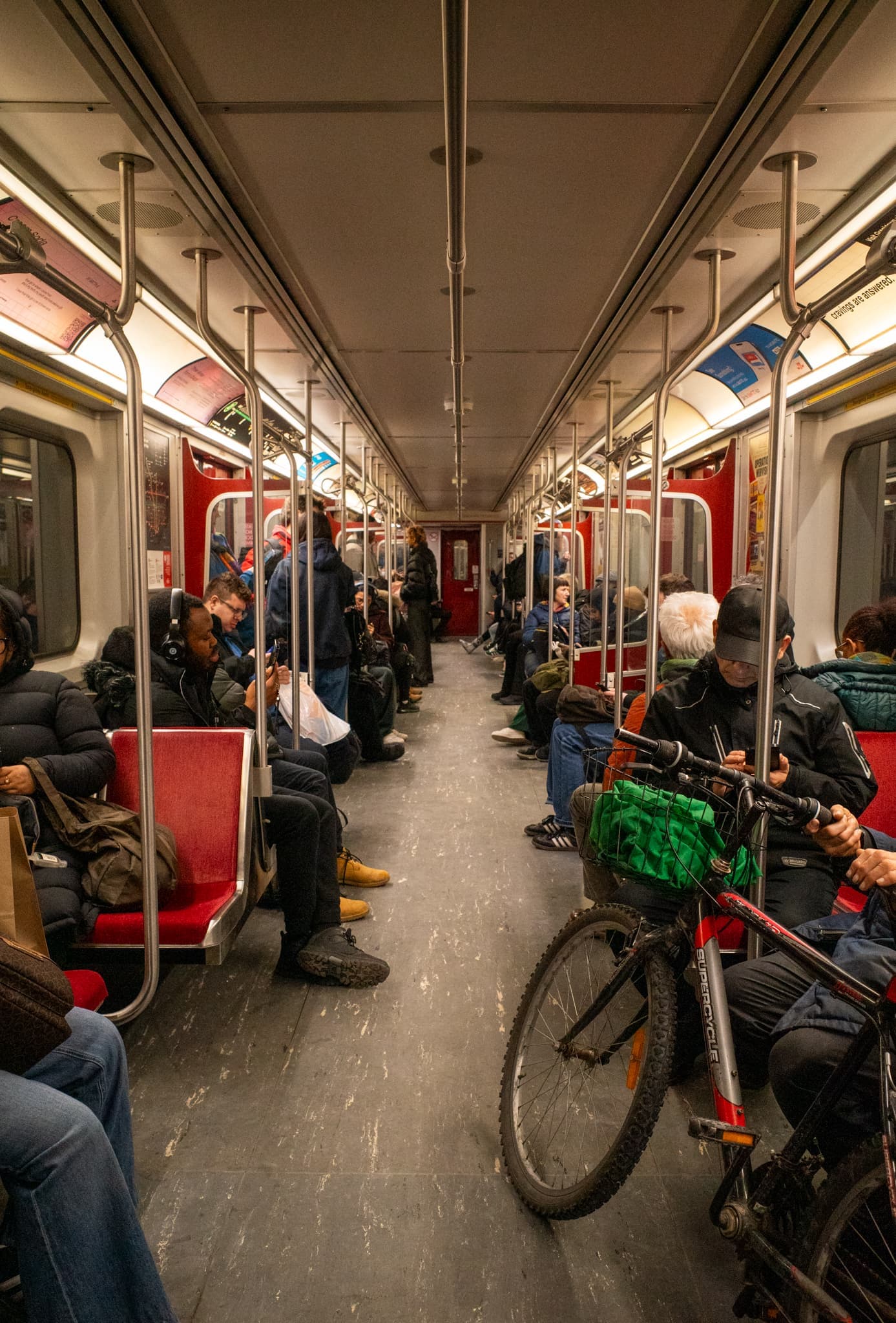 Passengers seated along both sides of a subway car interior, a green-basketed bicycle parked in the central aisle