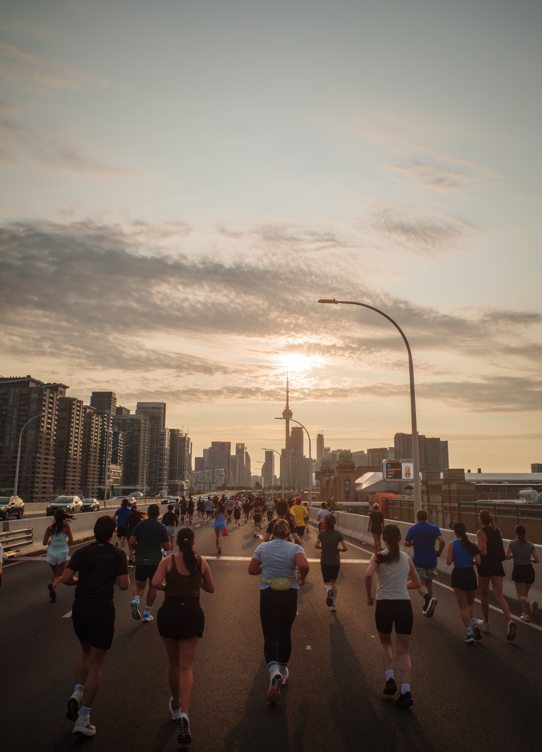 A pack of runners on a closed highway at sunrise, heading toward the Toronto skyline with the CN Tower straight ahead
