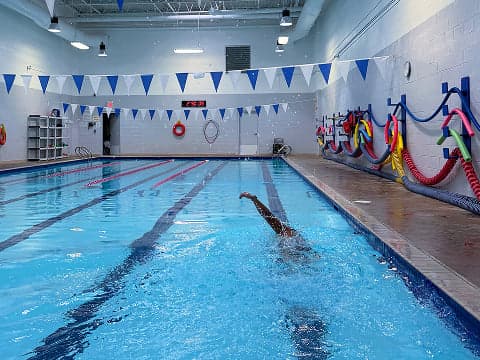 A swimmer doing laps in an indoor pool lined with lane ropes and triangular pennant flags