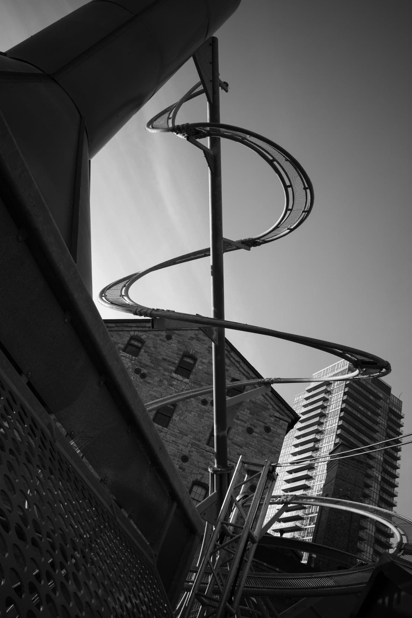 A spiral metal staircase winding around a central pole against a pale sky, in black and white