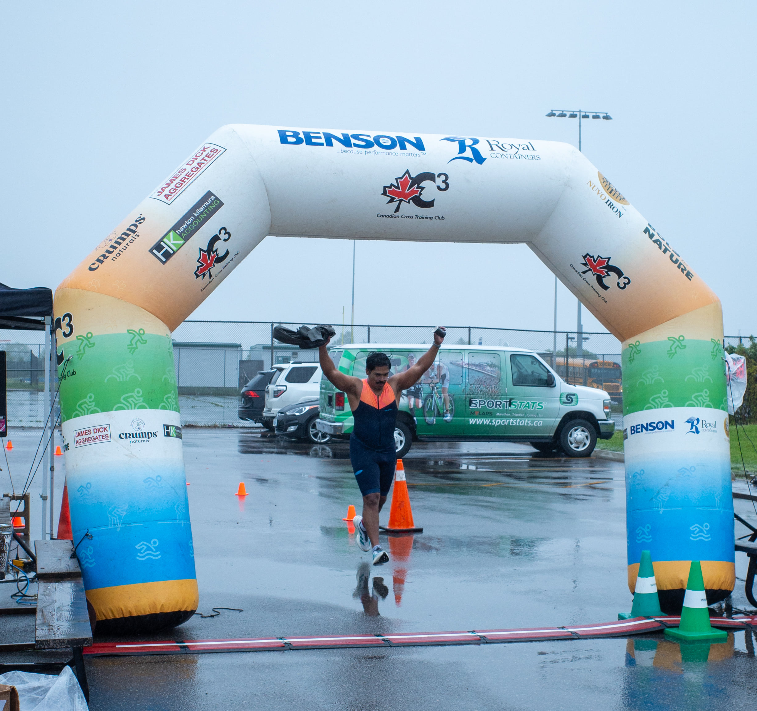 Crossing the finish line of a triathlon in the rain, arms raised